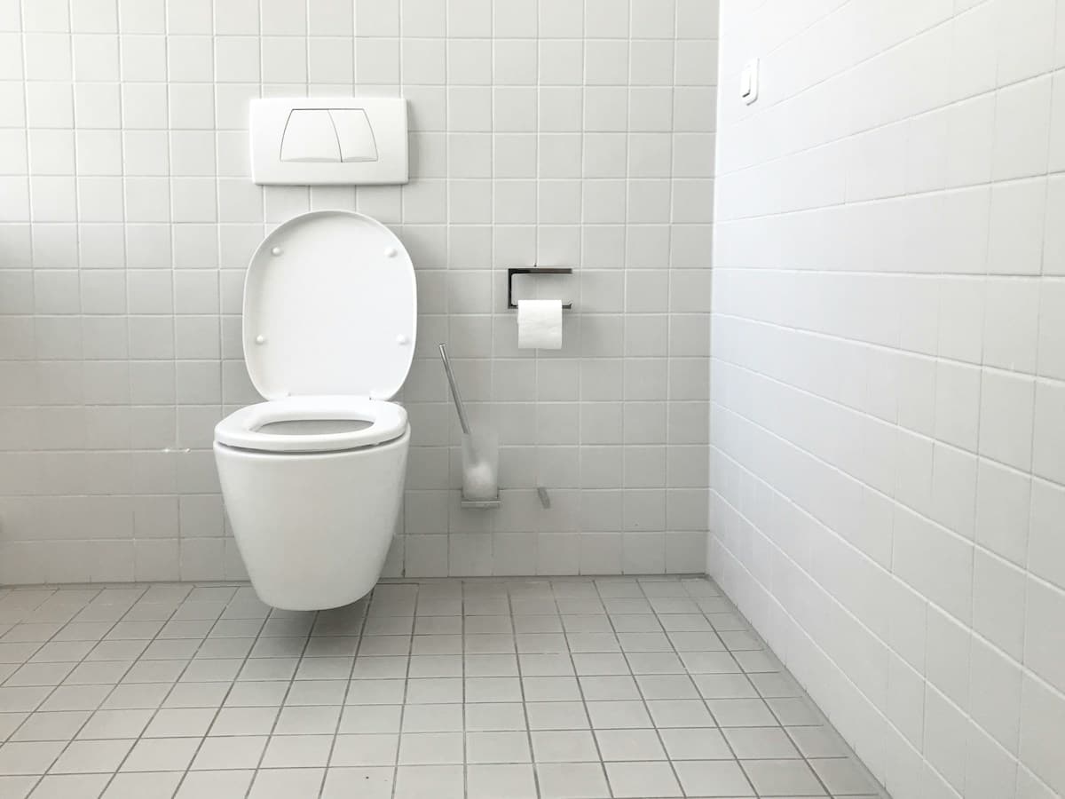 Et væghængt toilet med betjeningsplade på en hvid flisevæg